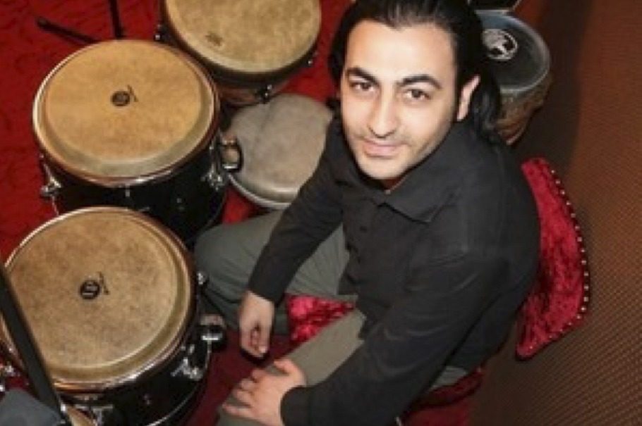 Ercan Dursun, souriant, assis derrière ses congas et ses tablas