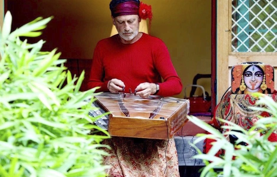 Jean-Marc Zelwer, en pull rouge, jouant du santour au milieu des plantes